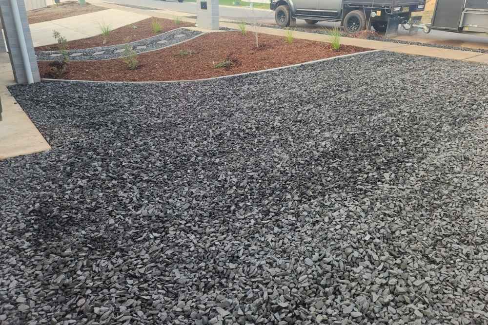 Landscaped garden bed featuring dark grey crushed gravel, mulch, edging, and young green plants in San Isidore-